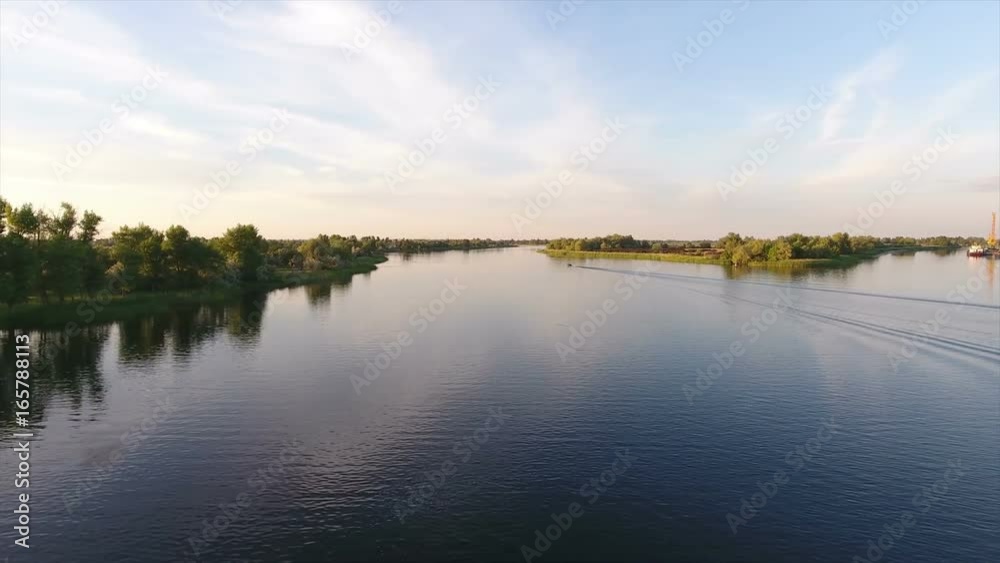 Exciting view on the Dnipro river and its picturesque blue waters at sunset in summer. The riverbanks are covered with greenary and look gorgeous and great. The skyscape is blue and transparent
