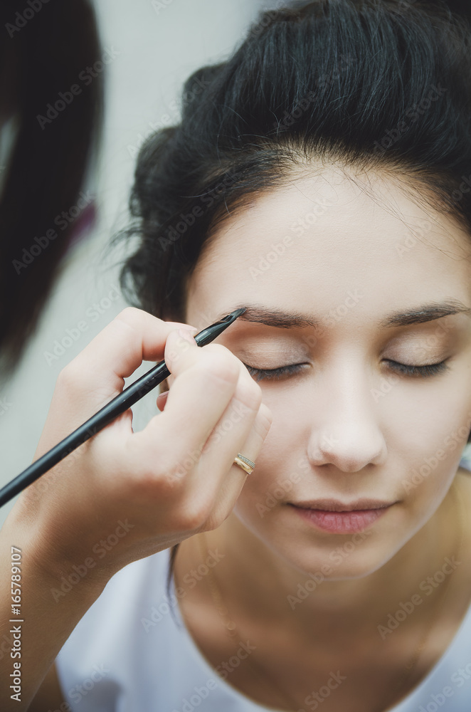 Make-up artist paints eyebrows to girl brunette, close-up.