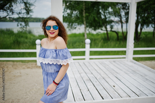 Portrait of a fabulous young girl wearing chic outfit posing on a white wooden terrace.