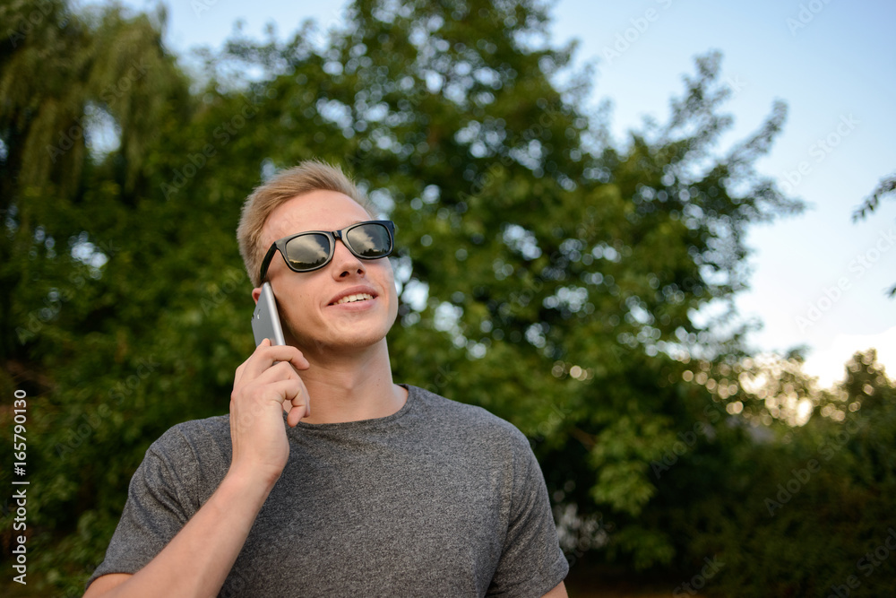 A young guy in glasses is talking on the phone and walking in the park A young guy in glasses is talking on the phone and walking in the park