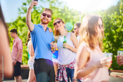 Happy couple taking selfie with smartphone at outdoor party