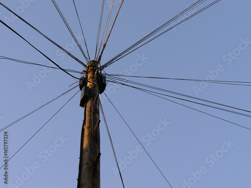 Telephone and electricity pole with wires against a blue sky