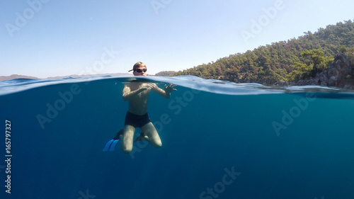 Half underwater close up, swimmer in flippers dives into the sea
