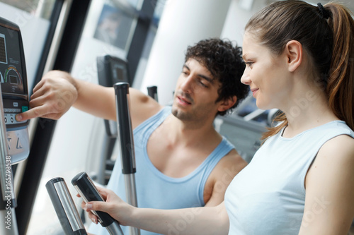 Trainer helping woman on exercise stepper machine.