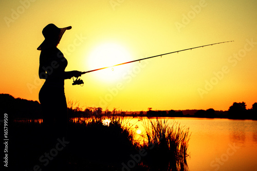 Silhouette of a woman in a hat engaged in sport fishing