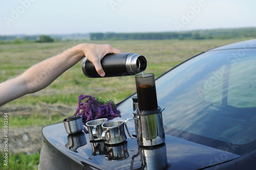 Items for alternative brewing of coffee in travel on the trunk of a black car. Summer landscape in the field