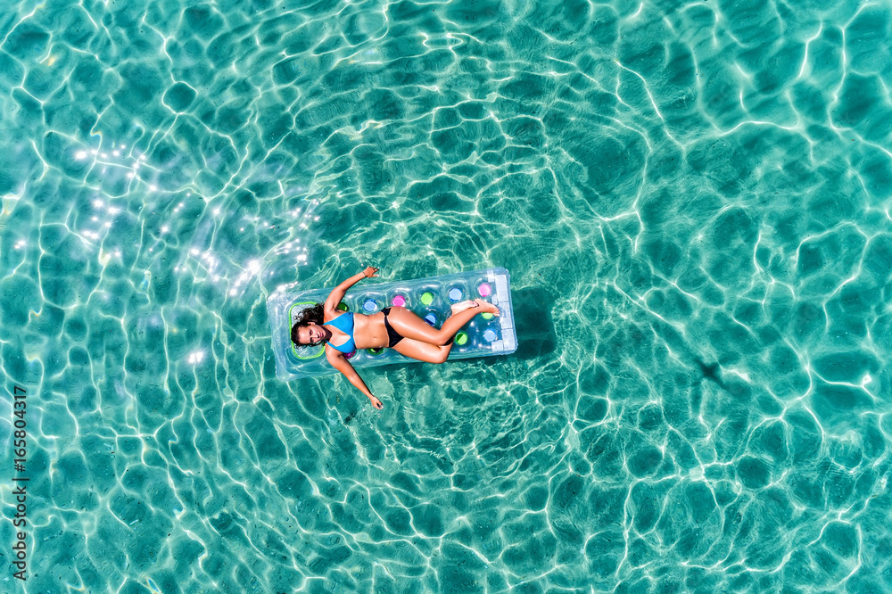 aerial view  of a beautiful young woman in bikini on a matress in the sea