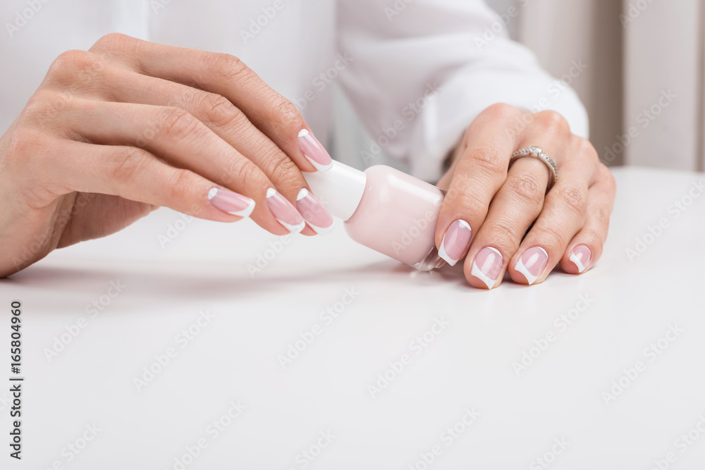 cropped shot of woman holding nail polish while doing manicure cropped shot of woman holding nail polish while doing manicure