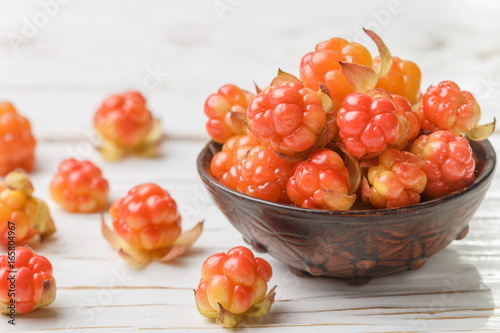 Fresh organic Berry cloudberries in a clay bowl on light wooden background. Selective focus