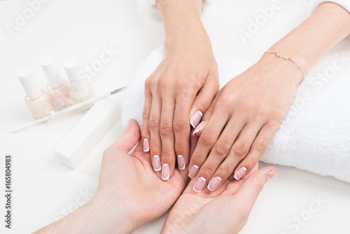 cropped shot of manicurist holding female hands with beautiful french manicure