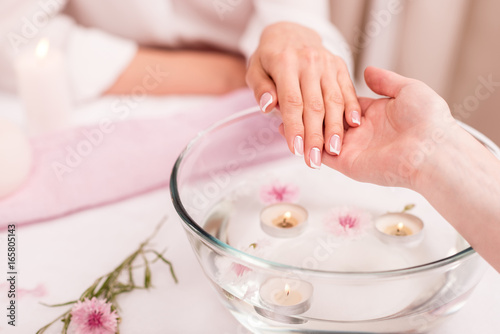 cropped shot of woman receiving spa treatment for hands in glass bowl with rose petals