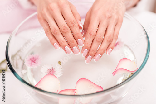 close-up view of female hands receiving spa treatment in glass bowl with rose petals
