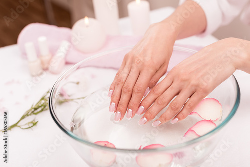 close-up view of female hands receiving spa treatment in glass bowl with rose petals