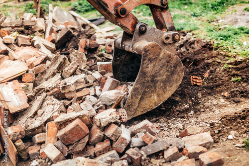 backhoe excavator demolishing building and gathering debris during house construction