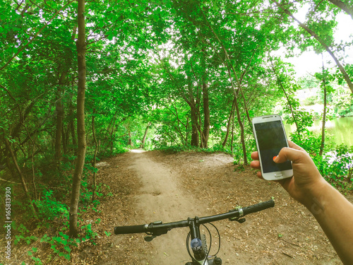 A man cyclist stands in the forest on a dirt road with a bicycle and holds a telphone in his hand. Copy space. photo