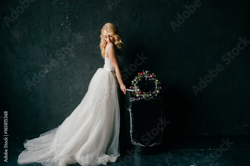 Pinup style portrait of beautiful elegant bride in expensive italian stylish wedding dress showing artisctic emotions on black texture wall background. Cute girl with slender posture and slim body. photo