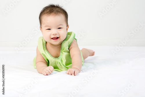 Portrait of a little adorable infant baby girl with saliva lying on the tummy on bed and looking in camera indoors