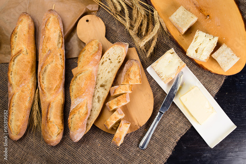 still life with French fresh bread baguettes with poolish on a wooden cutting board, butter and wheat. Shallow dof, flat lay