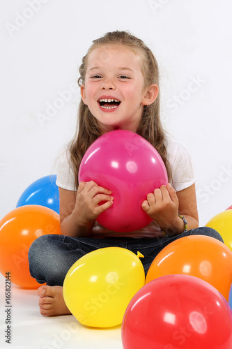 Kleines Mädchen sitzt zwischen Ballons und lacht