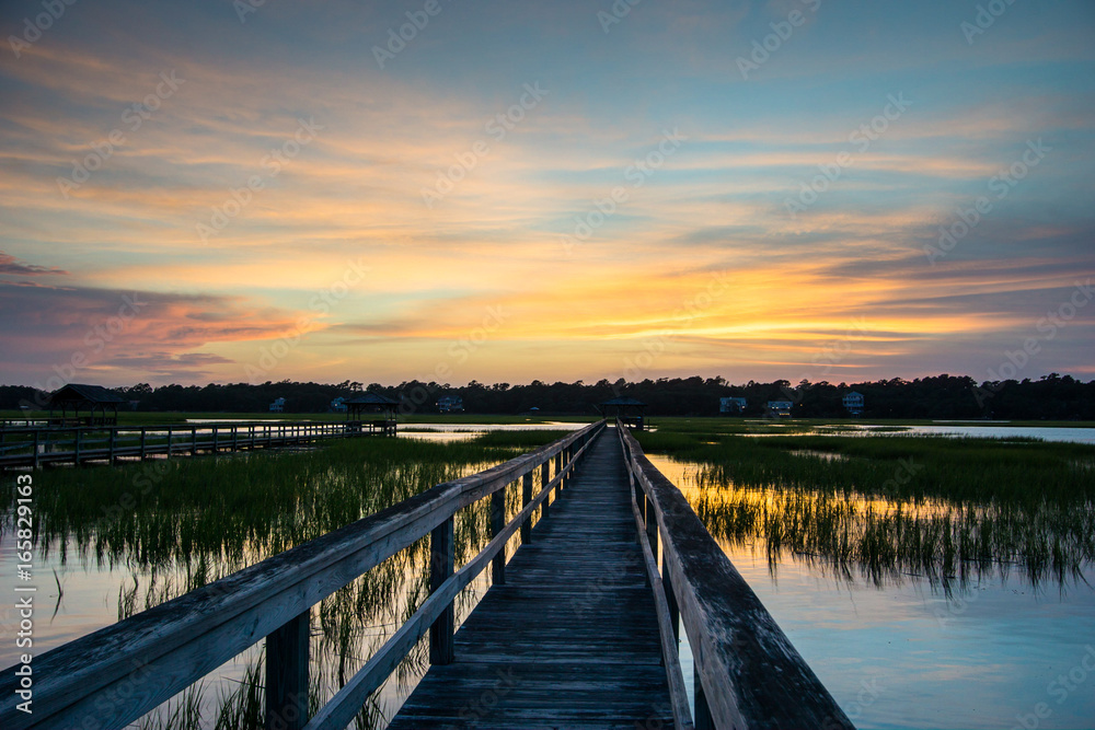 boardwalk leading into tidal basin of a barrier island filled with marsh grass under a beautiful sky at sunset in South Carolina