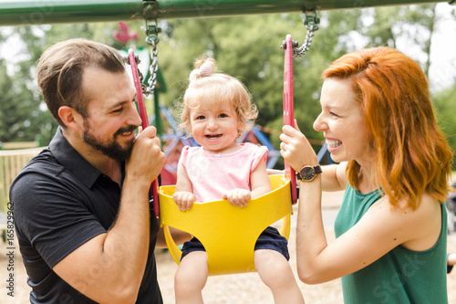 Father, mother with their daughter have fun on a swing