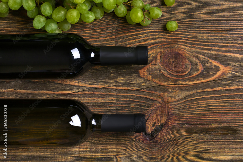 Obraz premium Bottles of wine and ripe grapes on wooden background