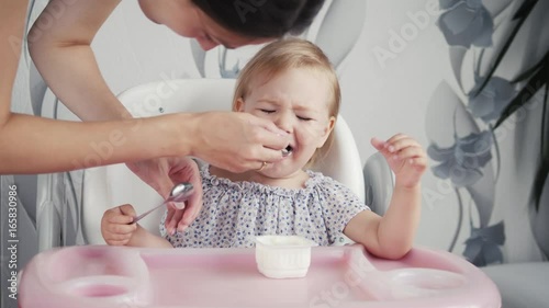 baby eating food on kitchen with mother, little baby girl first eat with mom, healphy food photo