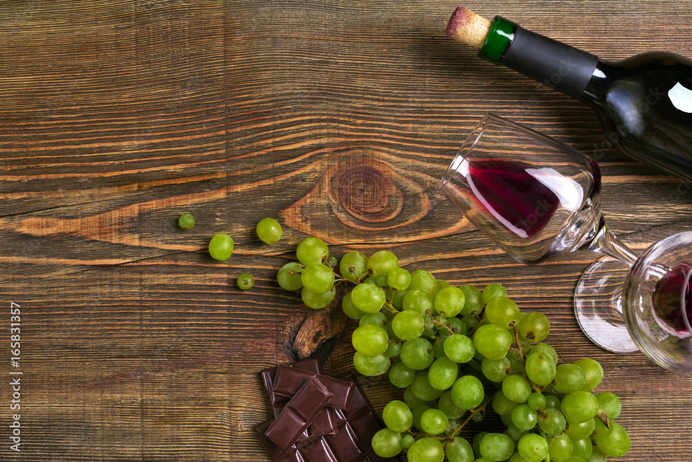 Obraz premium Two glasses, bottle of red wine and grape on a wooden table