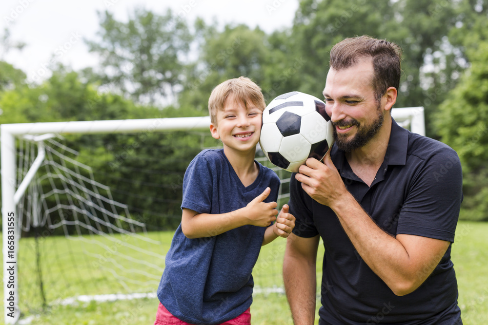 Naklejka premium Young father with his little son playing football on football pitch
