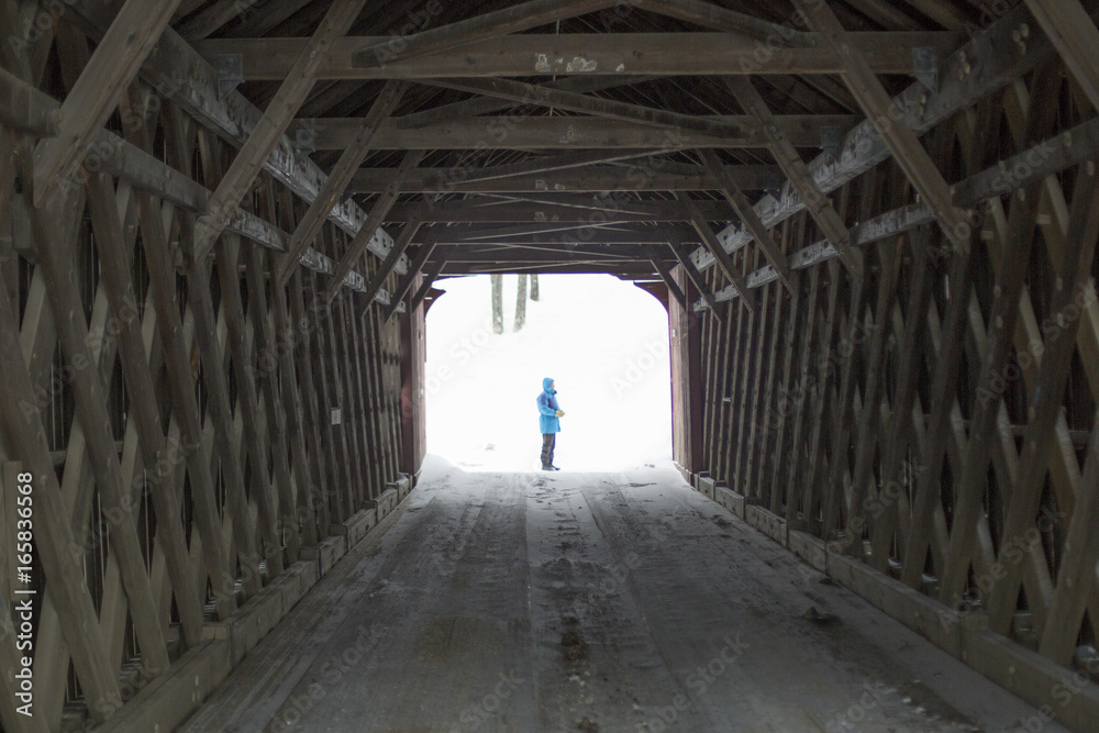 Looking through a covered wooden bridge at a man in winter in New England