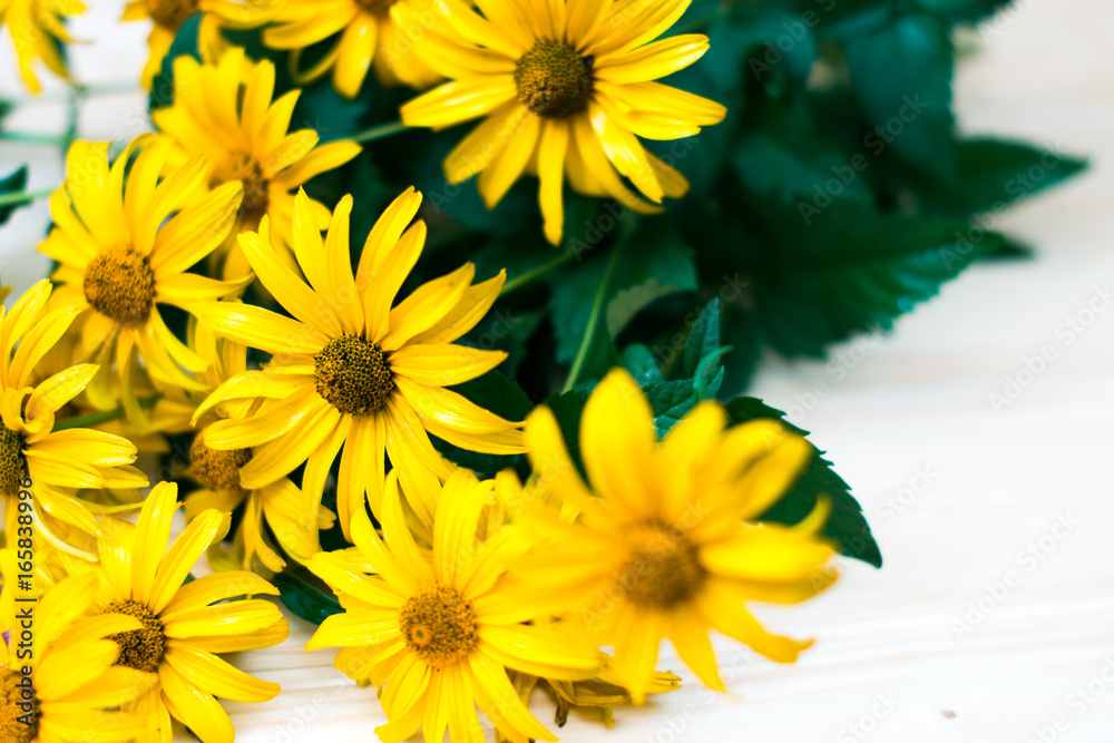 Obraz premium Yellow flowers on a wooden table with blurred background.