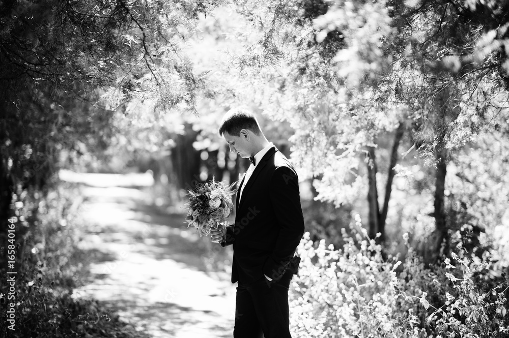 Portrait of a handsome groom holding his wife's bouquet walk in the park.  Black and white photo.