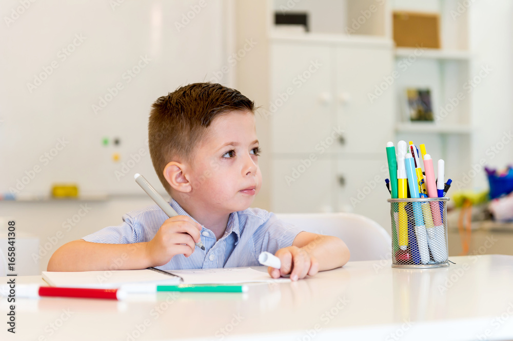 child preschooler boy drawing on booklet ,while sitting on the desk in the classroom child preschooler boy drawing on booklet ,while sitting on the desk in the classroom