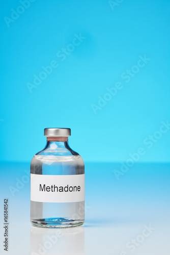 (English label in transverse format) A ampoule of methadone stands on white surface against gray background on the left. Iin portrait format with plenty of space for text