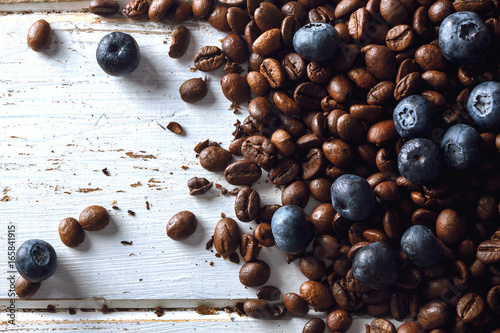 Roasted coffee beans with blueberries over a white wood table
