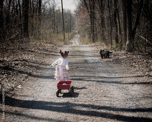 cute little girl pulling wagon with dog on wooded lane