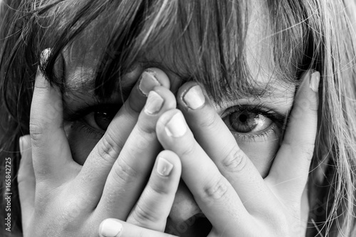 Conceal and reveal: Black and white close up portrait of a young girl hiding behind her hands