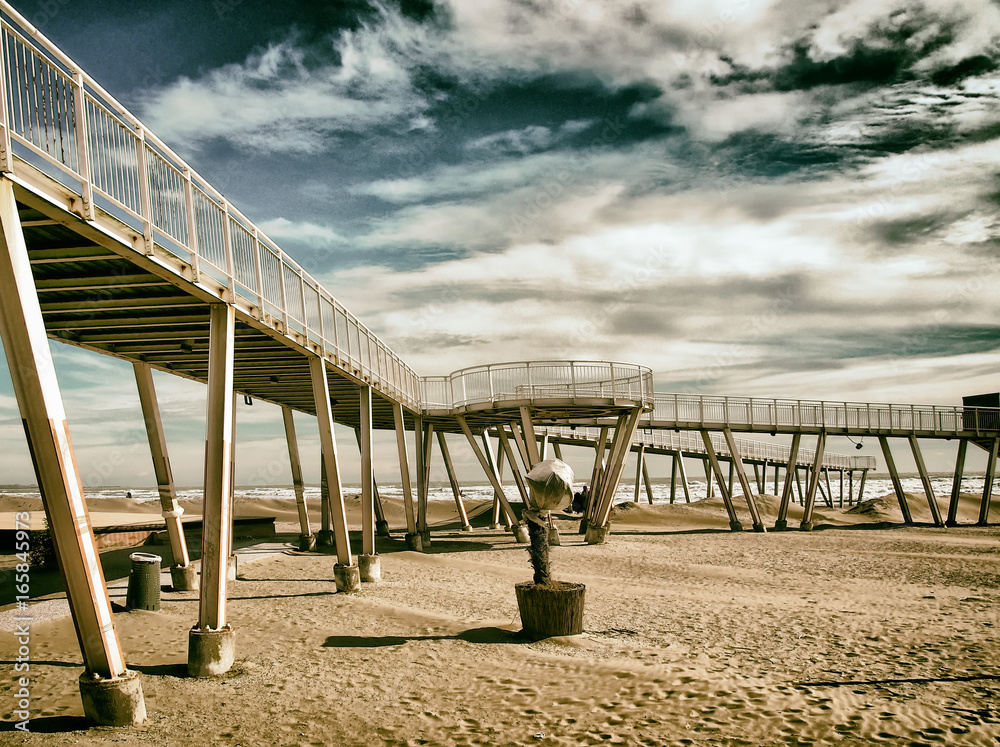 beach at the lido in venice with metal modern pier and elevated walkways with dramatic sky sea and sand out of season.
