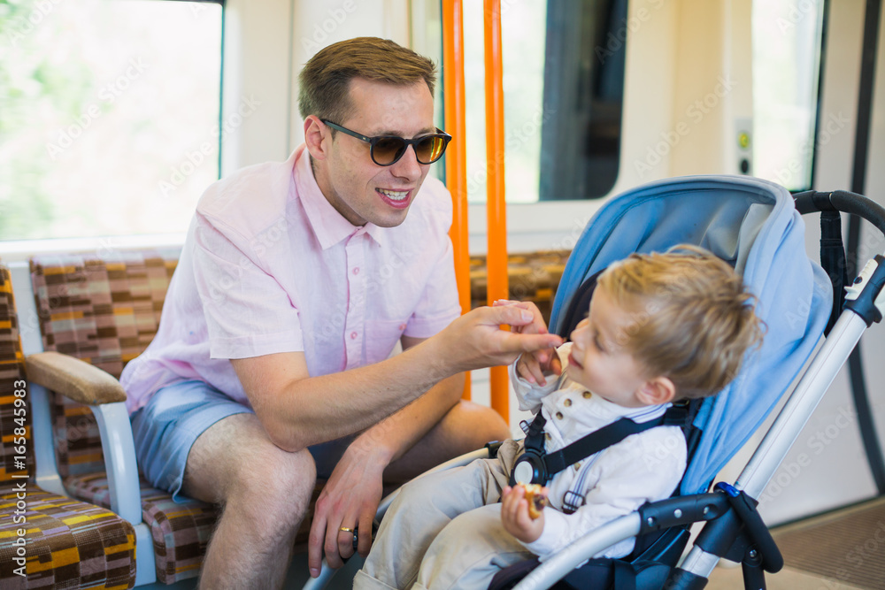 Obraz premium The young handsome father sits in a bus and plays with his little son