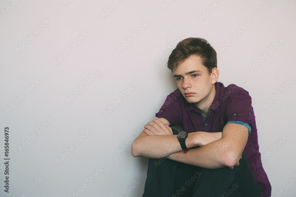 Lonely, sad, tired teenager sitting on the floor in an empty room