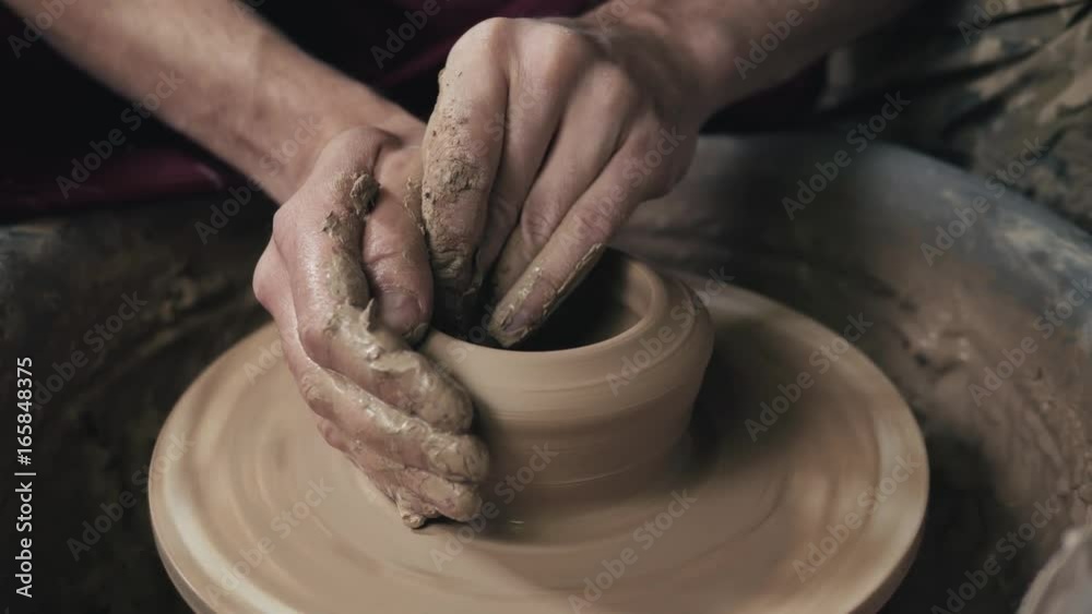 The hands of a potter, creating an earthen jar on the circle, close-up, hands on circle with clay