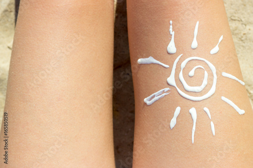 Woman sunbathing on the beach with a drawing of sun on her leg with cream