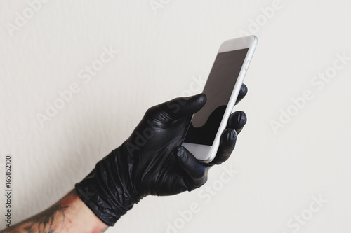 Tattooed man in black glove using white smartphone