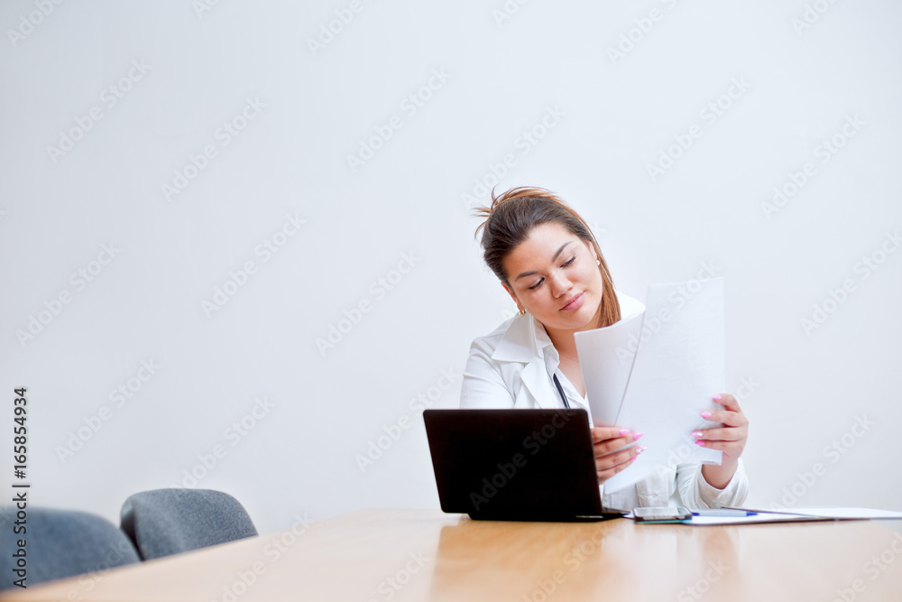 Young female hispanic doctor sitting behind the desk looking into a paper forms Young female hispanic doctor sitting behind the desk looking into a paper forms