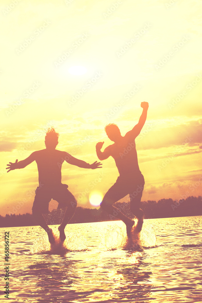 Fototapeta premium Glückliche junge Menschen laufen und springen am See beim Sonnenuntergang