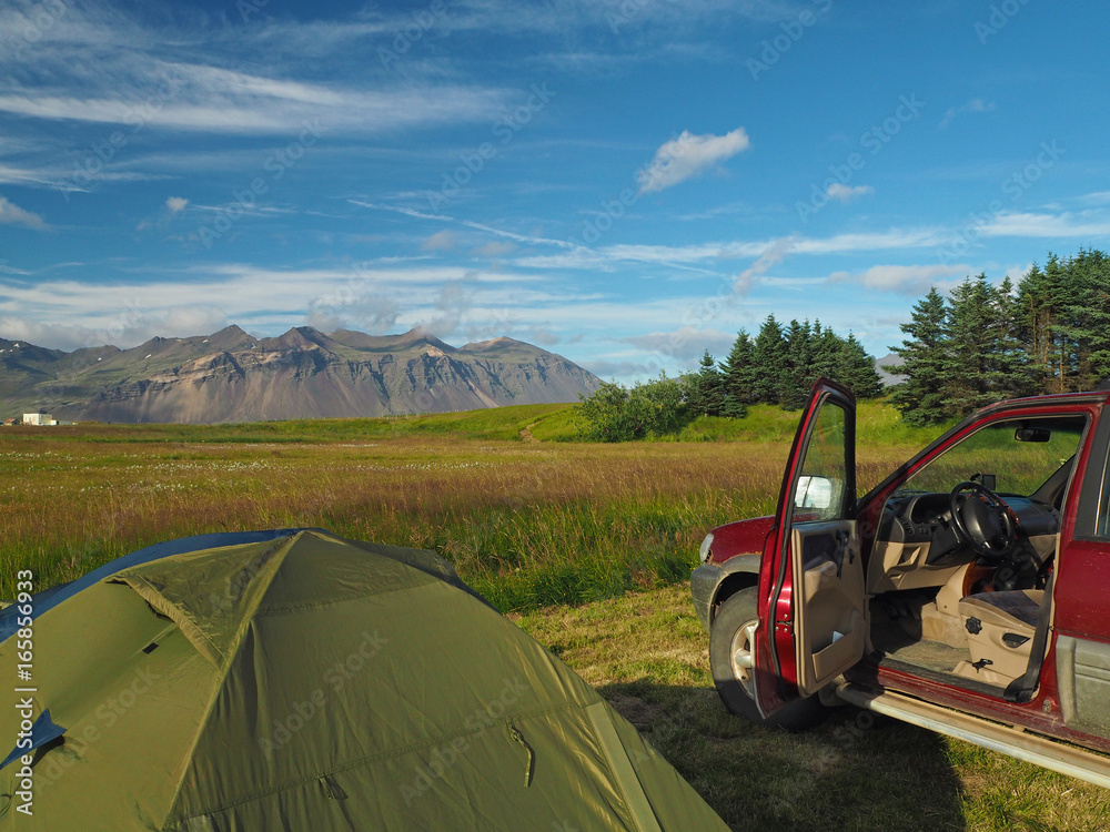 camping adventure in Iceland - tent and old off-road car with open door - view on colorful mountains meadow and trees