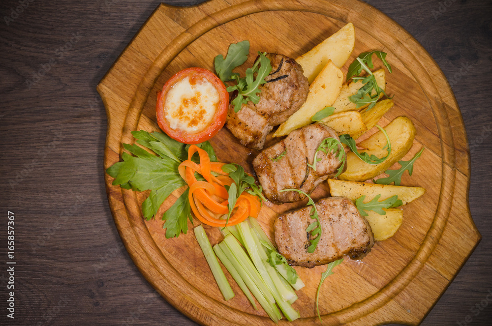 Three pork steaks with fried potatoes and vegetables on a wooden background Three pork steaks with fried potatoes and vegetables on a wooden background
