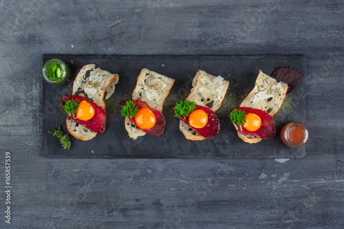 Four tiny appetizers with cured met, yolk and parmegano cheese on stone board with copyspace. Top view photo