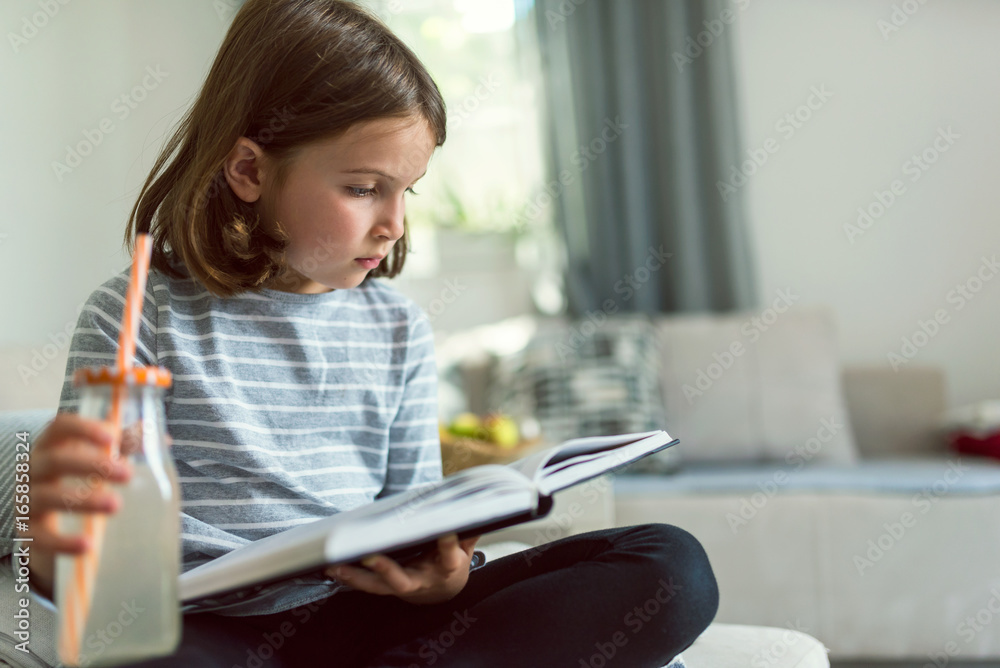 Cute young girl reading exciting book and drinking lemonade at home Cute young girl reading exciting book and drinking lemonade at home