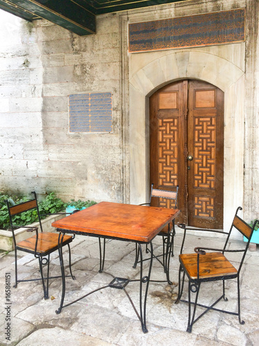 Metal and wooden table with two Arabic style chairs in front of the mosque wooden door